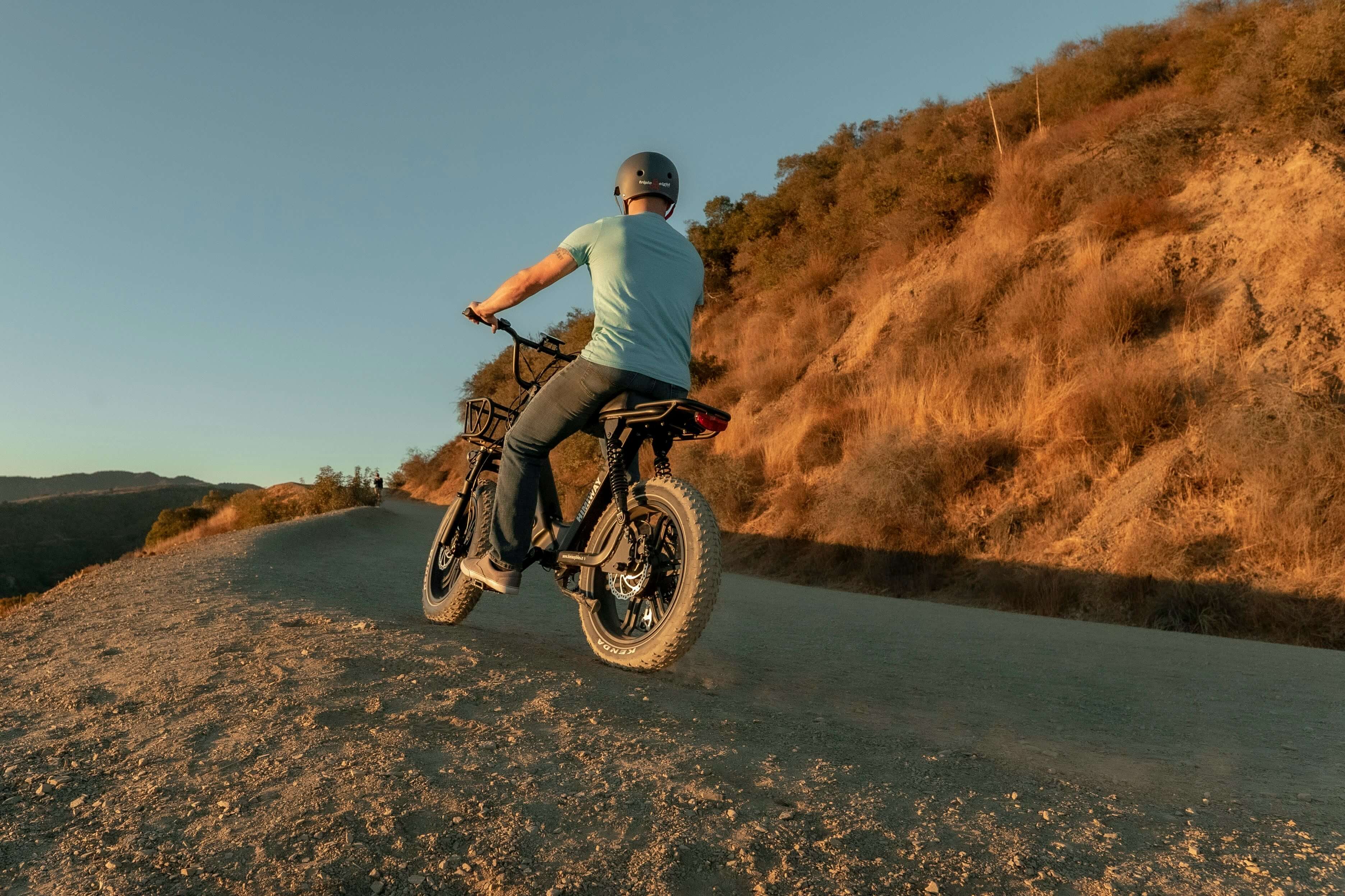 A rider climbing a scenic mountain road on a black Univercycle folding e-bike, demonstrating the climbing performance and high-torque capabilities of the motor.