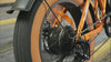 A close-up video showing the rapidly spinning rear wheel of the orange Univercycle Urano electric bike, showcasing its powerful 1000W rear hub motor and Shimano 7-speed derailleur drivetrain